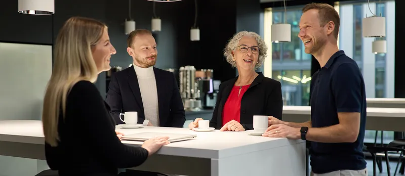Zwei Frauen und zwei Männer stehen an einem Hochtisch und unterhalten sich. 