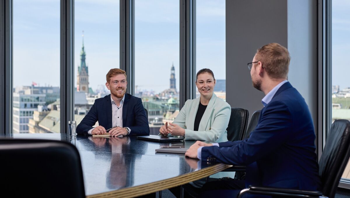 Drei Trainees sitzen an einem runden Tisch mit Ausblick auf die Stadt.