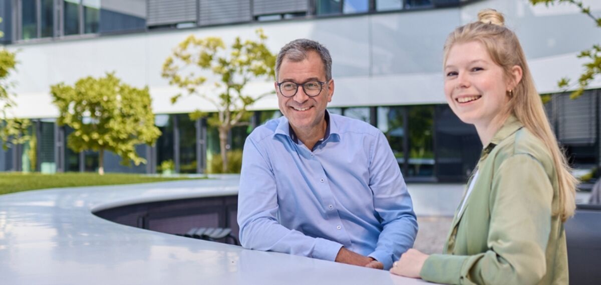 Ein Mann und eine Frau stehen an einem Hochtisch in einem grünen Innenhof.