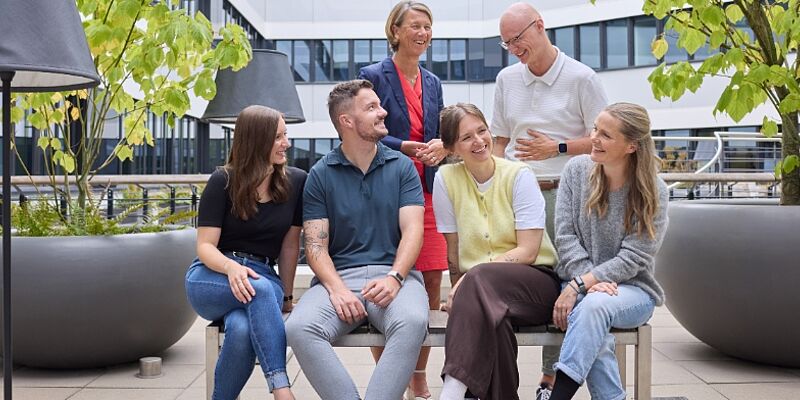 Sechs Personen sitzen und stehen im grünen Innenhof und unterhalten sich. 