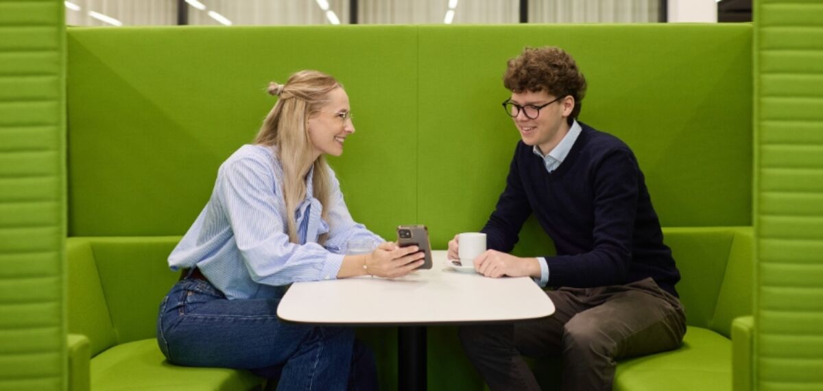 Zwei dual Studierende sitzen in einer grünen Lounge Ecke und unterhalten sich. 