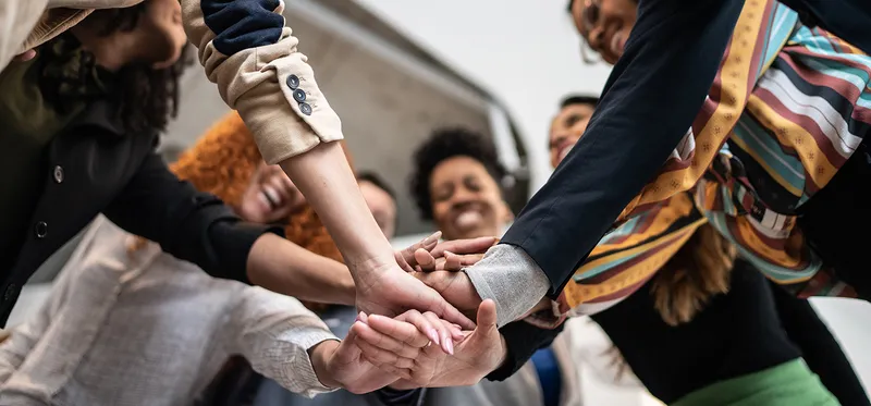 Mehrere Menschen, die im Kreis stehen und die Hände zusammenlegen