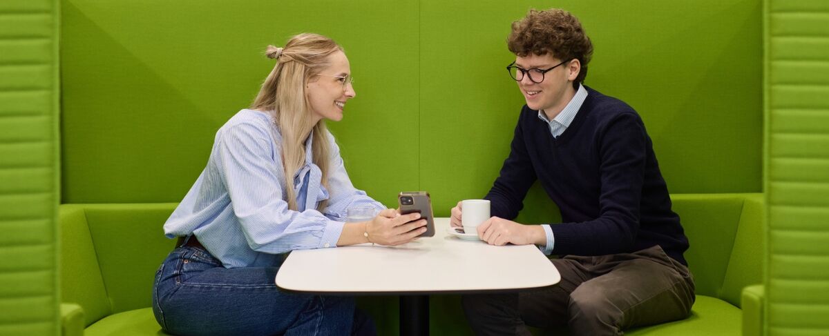 Duales Studium bei der DZ HYP Zwei duale Studenten sitzen in einer grünen Sofaecke und unterhalten sich.