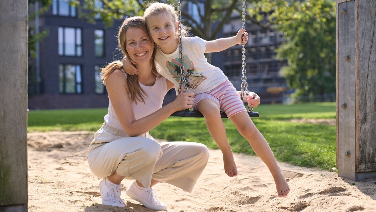 Was wir bieten - Vereinbarkeit von Beruf und Privatleben Eine Frau und ihre Tochter befinden sich auf einem Spielplatz, das Kind sitzt dabei auf der Schaukel.