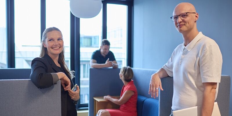 Vier Personen befinden sich in einer Gesprächssituation, zwei von ihnen schauen freundlich in die Kamera.