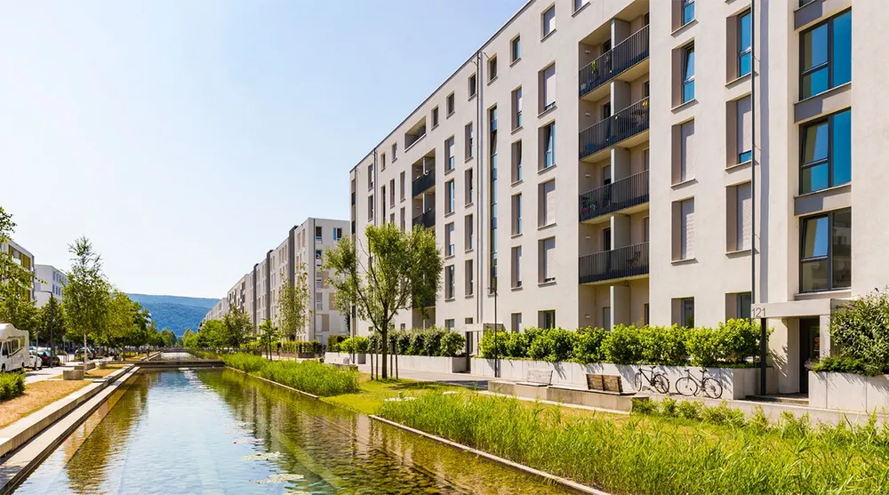 Titelausschnitt DZ HYP Green Bond Report 2024 - Mehrfamilienhäuser an einem Wasserlauf vor blauem Himmel Titelausschnitt DZ HYP Green Bond Report 2024 - Mehrfamilienhäuser an einem Wasserlauf vor blauem Himmel