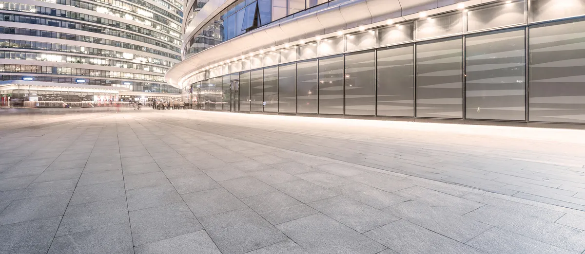Moderne Glasfassade mit beleuchtetem Vorplatz bei Nacht