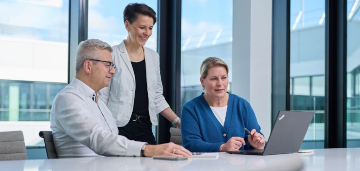 Drei Personen sitzen an einem Tisch vor einem Laptop