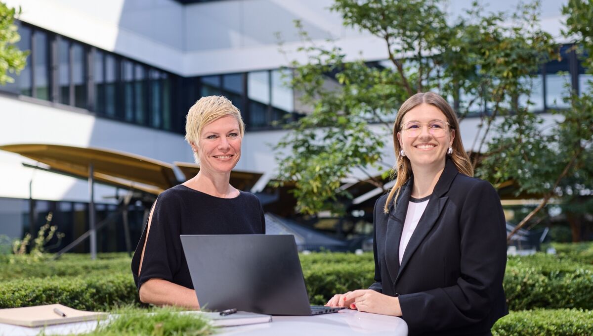 Zwei Frauen stehen mit einem Laptop in einem grünen Innenhof