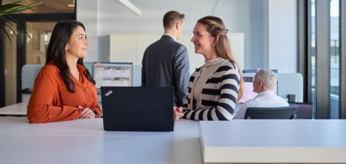 Zwei Kolleginnen stehen an einem Schrank und unterhalten sich in einem Büro.